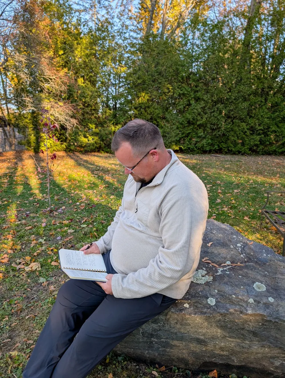 Ben Frazier sitting on a rock at golden hour, writing in a spiral notebook.